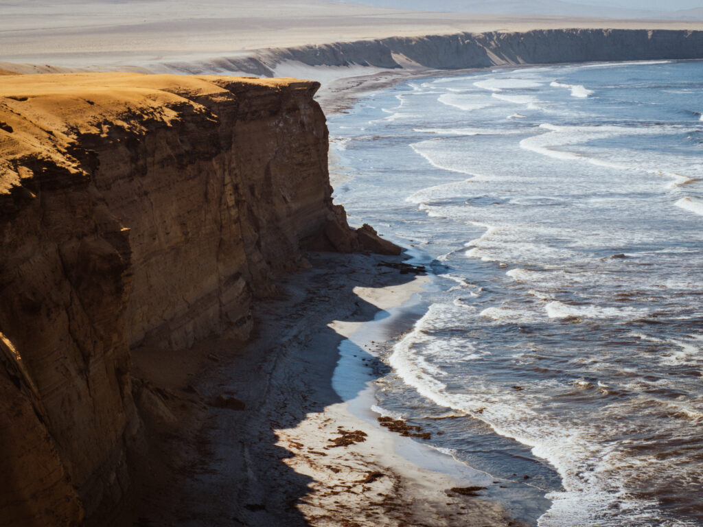 Cliffs and shoreline at Supay Beach in Paracas National Reserve, Peru, where desert meets ocean under golden light.