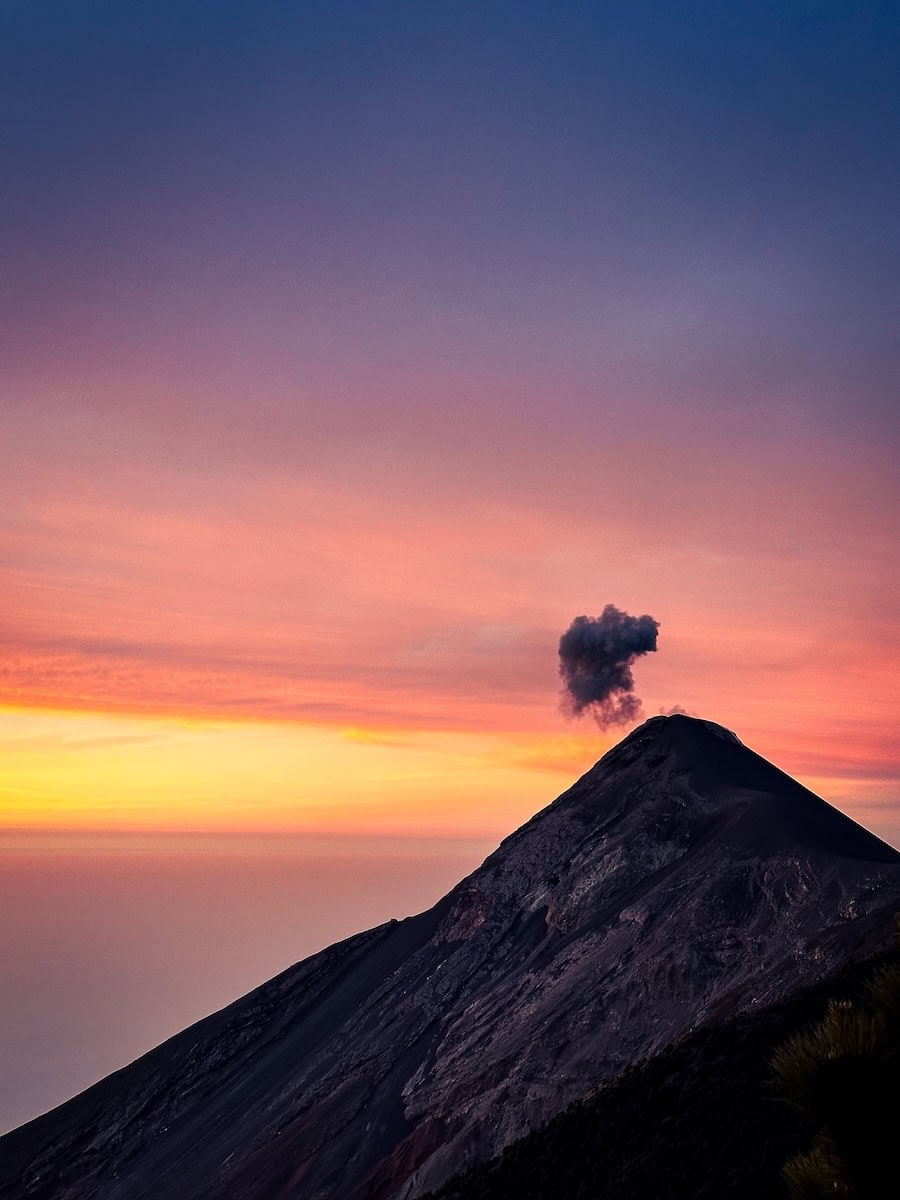Volcán de Fuego erupting at sunrise with a plume of smoke against a vivid pink and orange sky in Guatemala, Central America